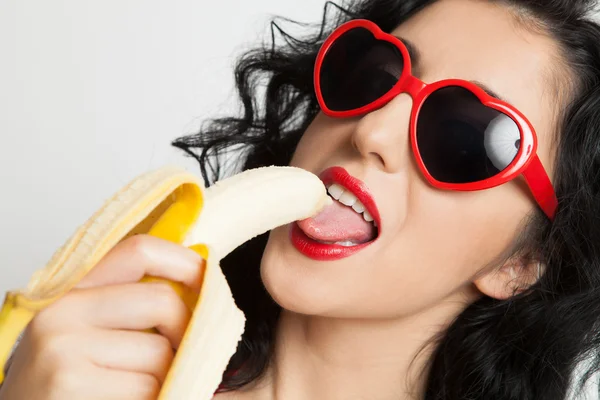 Hot brunette woman with red glasses sexy eating banana