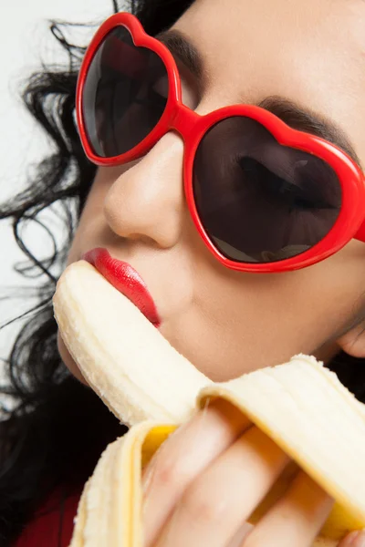 Mulher morena quente com óculos vermelhos sexy comer banana — Fotografia de Stock