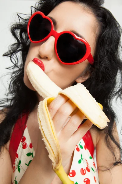 Hot brunette woman with red glasses sexy eating banana — Zdjęcie stockowe