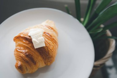 Kapalı sade kruvasan üzerine beyaz tabakta tereyağı.