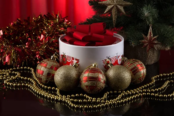 Christmas card. A gift box of chocolates and red-gold Christmas decorations on a dark reflecting surface next to the spruce.