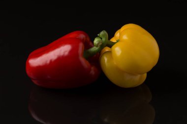 Çapraz saplı iki dolma biber, kırmızı ve sarı, siyah bir arkaplana karşı koyu bir yansıtıcı yüzeyde yatar..