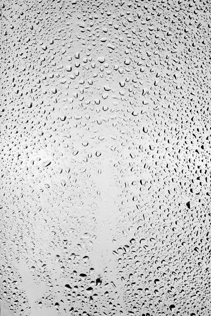 Drops of water flow down the surface of the clear glass on a gray background. Texture for creativity.