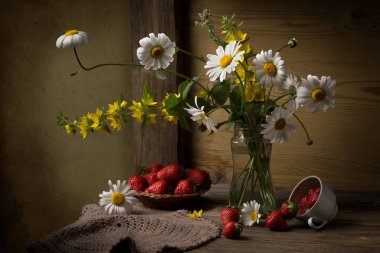 Bir buket papatya, cam bir kavanozda limachia çiçekleri ve masada çileklerle hayat..