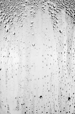 Su damlaları temiz camın yüzeyinden gri arka planda akar. Yaratıcılık için doku.