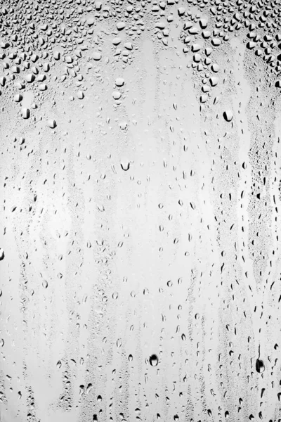 Su damlaları temiz camın yüzeyinden gri arka planda akar. Yaratıcılık için doku.