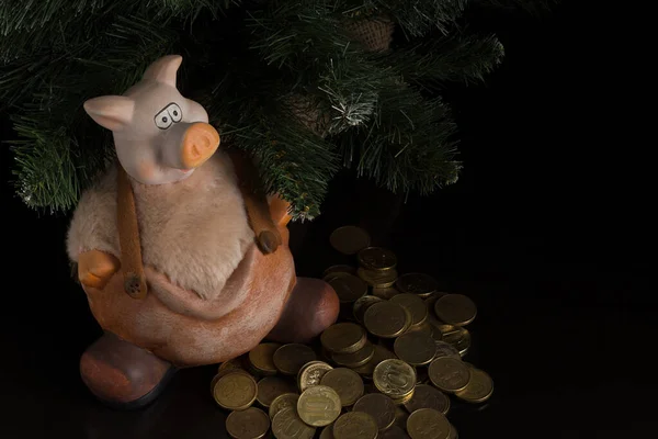 Masanın üzerinde, Noel ladininin altında stilize edilmiş domuz kumbarası var. Pantolon, bot ve bir avuç bozuk para şeklinde. Yukarıdan görüntüle.