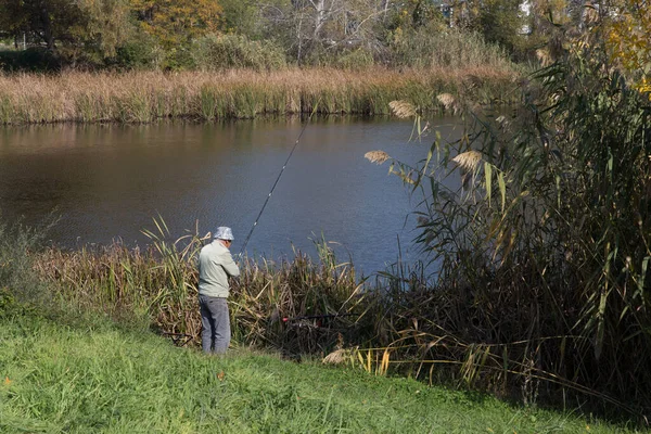 Açık bir sonbahar gününde göl kıyısında elinde olta kamışlarıyla gezen bir adam..