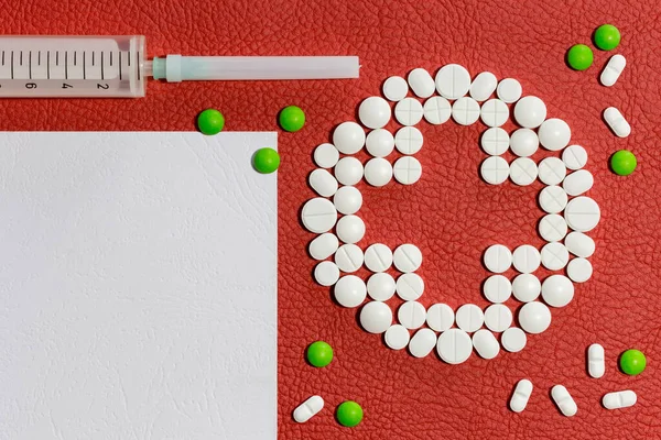 Tıbbî tabletlerden, bir şırıngadan ve kırmızı yapay deri yüzeyinde boş bir kağıt tabakasından yola çıkarak dizilmiş. Tarif için şablon.