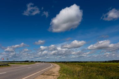 Kümülüs bulutları mavi gökyüzünde bir tarla çimenleri ve bir karayolu olan vahşi bir arazinin üzerinde. Gökyüzü deseni.