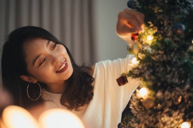 Kadın evdeki Noel ağacını süslüyor. Gülümseyen genç kadın Noel 'i kutluyor, Mutlu Noeller ve yeni yıl arifesi konsepti.