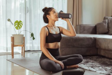 Evdeki eğitimden sonra evde oturup su içen bir kadın. Evde egzersiz yapan genç bir kadın..
