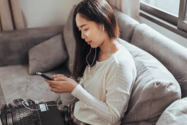 Akıllı telefon kullanan ve evde oturan genç bir kadın. Evde çalışırken cep telefonu kullanan güzel bir iş kadını. Coronavirus ya da Covid-19 karantinası sırasında evde çalışmak.