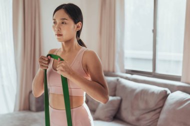 Evde direniş bandıyla egzersiz yapan genç bir kadın. Oturma odasında egzersiz yapan sağlıklı bir kadın. Ev egzersizi.