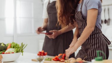 Mutfak odasında biber kesen romantik çiftin görüntüsü. Mutlu çift birlikte yemek yapmayı ve mutfakta online yemek kitabı izlemeyi sever..