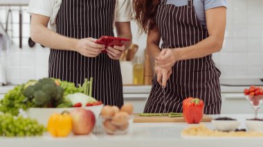 Mutfak odasında biber kesen romantik çiftin görüntüsü. Mutlu çift birlikte yemek yapmayı ve mutfakta online yemek kitabı izlemeyi sever..