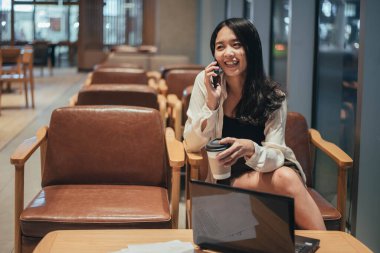 Geceleri akıllı telefon kullanan mutlu bir kadın. Asyalı iş kadını gece fazla mesai yaparken telefon kullanıyor..