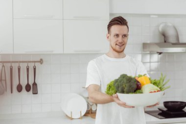 Mutfakta sebze tutan sağlıklı bir adam. Sağlıklı yemek pişirmek için sebze ve meyve gösteren mutlu genç adam..
