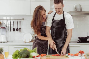 Mutlu çift mutfakta birlikte yemek yapmaya bayılır. Genç adam ve kadın evde sağlıklı yemek pişirirken gülüyorlar..
