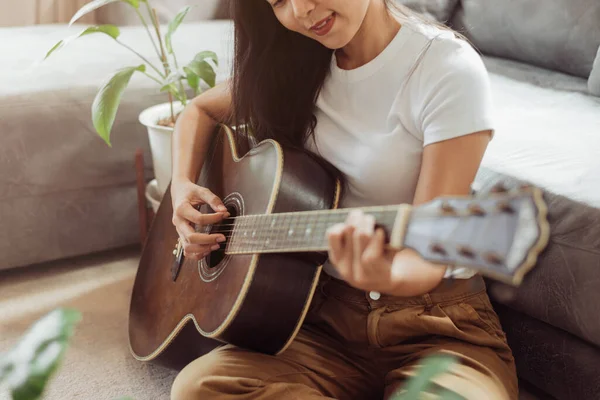 Woman playing guitar at home. Beautiful woman smiling and playing guitar with her plants in living room.