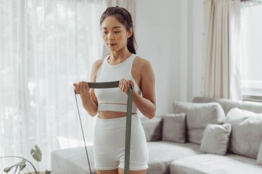 Evde direniş bandıyla egzersiz yapan genç bir kadın. Sağlıklı bir kadın oturma odasında çalışıyor. Ev egzersizi.
