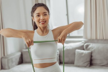 Evde direniş bandıyla egzersiz yapan genç bir kadın. Sağlıklı bir kadın oturma odasında çalışıyor. Ev egzersizi.