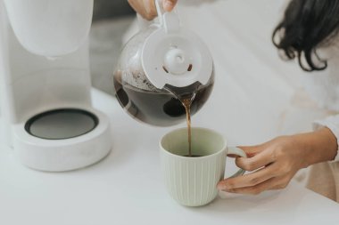 Genç mutlu kadın evde kahve makinesi kullanıyor. Asyalı kadın bir fincana kahve doldurup evde kahve yapıyor..