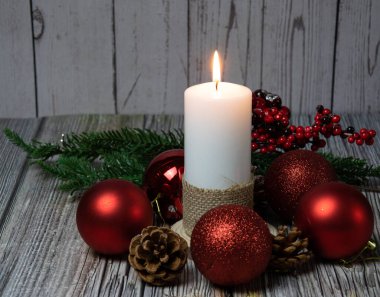 Kozalaklı mumlar, köknar dalları ve ahşap arka planda kırmızı toplar.