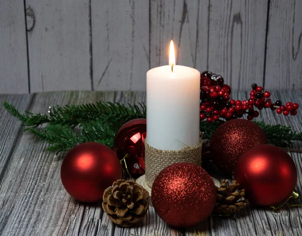 Kozalaklı mumlar, köknar dalları ve ahşap arka planda kırmızı toplar.