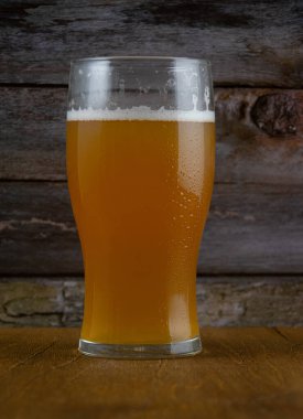 Bir bardak filtresiz bira, beyaz köpüklü ahşap bir masa.