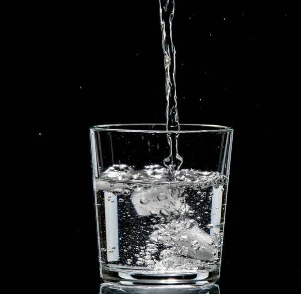 Vidro transparente com gelo e água. A água é derramada em um copo — Fotografia de Stock