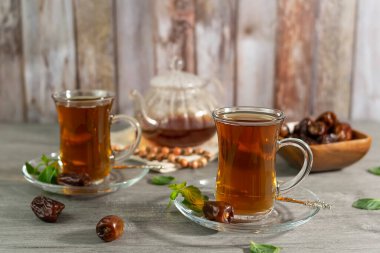 Tahta bir masada Türk fincanlarında güzel kokulu çay. Arka planda nane yaprakları, yıldız anason ve tarçın tüpleri