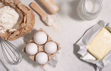 Yumurtalar, un torbada, tereyağı pakette, süt de parlak bir masada. Hamur yapmak için gerekli malzemeler. Üst görünüm