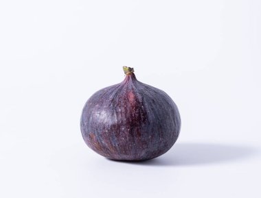 Beyaz bir masanın üzerinde mor, yuvarlak bir incir duruyor. İzole edilmiş arkaplan