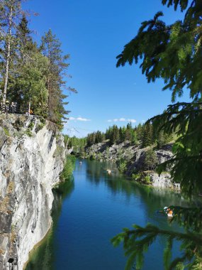 Ruskeala Dağ Parkı 'ndaki Mermer Kanyon' un turkuaz suyunun gözlem güvertesinden gökyüzünün yansıması ve güneşli bir yaz gününde ağaçların görüntüsü..