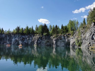 Güneşli bir yaz gününde Ruskeala Dağ Parkı 'nda turistlerin yüzdüğü Mermer Kanyon' un kayalık kıyıları ve turkuaz suları görülüyor..