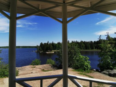 Vyborg şehrinin Monrepos Parkı 'ndaki Vyborg Körfezi' nin pitoresk sahilindeki Çay Çardağı 'ndan manzara bulutlu mavi bir gökyüzünün arka planına karşı.