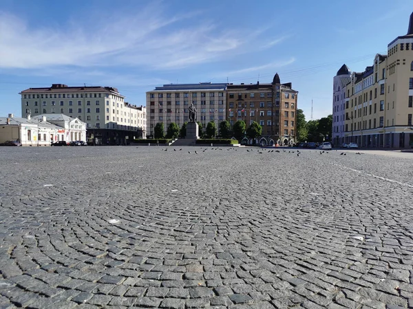 Red Square in the city of Vyborg, laid with paving stones, with a monument, surrounded by old houses.