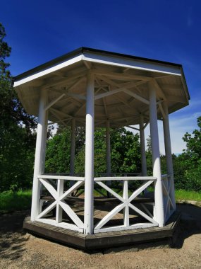 Vyborg şehrinin parkındaki Vyborg Koyu 'nun kıyısındaki bir dağda duran beyaz bir çay çardağı bulutlu mavi bir gökyüzünün arka planına karşı..