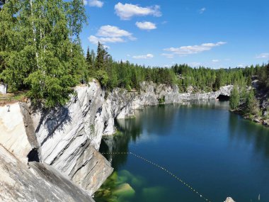 Güneşli bir yaz gününde Ruskeala Dağ Parkı 'ndaki Mermer Kanyon' un berrak turkuaz sularındaki kayalık kıyıları ve büyük kayaları görmek.
