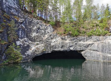Güneşli bir yaz gününde Ruskeala dağ parkında, mağaranın suyundan ve ağaçların yetiştiği su basmış Mermer Kanyon 'un yamacından manzara.