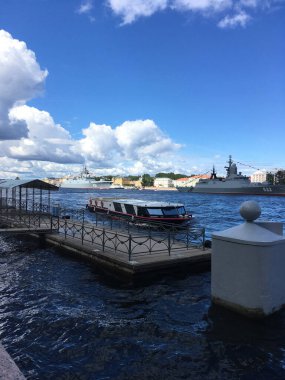 A pier, to which a pleasure boat approaches, followed by warships in the water area of the Neva, arrived to participate in a naval parade in St. Petersburg.