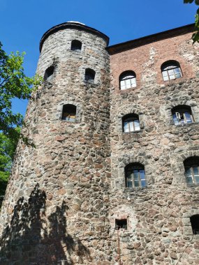 Vyborg şehrindeki Vyborg kalesinin dış taş duvarı ve kulesi mavi gökyüzünün ve ağaç dallarının arka planına karşı..