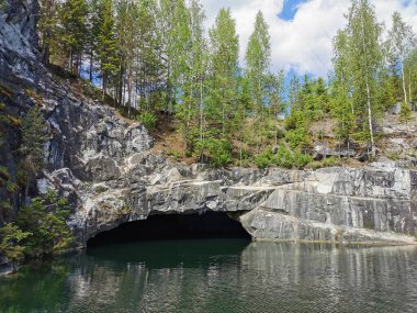 Güneşli bir yaz gününde Ruskeala dağ parkında, mağaranın suyundan ve ağaçların yetiştiği su basmış Mermer Kanyon 'un yamacından manzara.