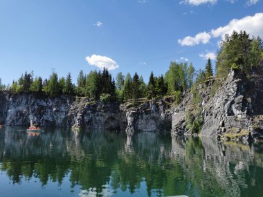 Güneşli bir yaz gününde Ruskeala Dağ Parkı 'nda turistlerin yüzdüğü Mermer Kanyon' un kayalık kıyıları ve turkuaz suları görülüyor..