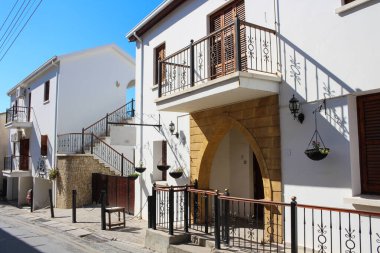 Bellapais köyünün boş bir caddesinde beyaz evler, işlenmiş demir parmaklıklar ve eve kemerli bir giriş. Kıbrıs.