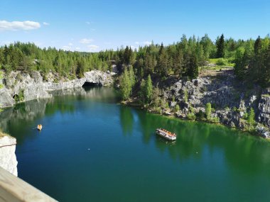 Ruskeala Dağ Parkı 'ndaki Mermer Kanyon' un turkuaz suyunun gözlem güvertesinden gökyüzünün yansıması ve güneşli bir yaz gününde ağaçların görüntüsü..