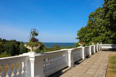 Beyaz bukleli çitleri, ağaçları ve parlak mavi gökyüzüne karşı bir saksısı olan bir teras. Baltık Denizi manzarası. Oru. Estonya.