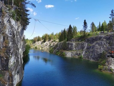 Güneşli bir yaz gününde Ruskeala Dağ Parkı 'ndaki Mermer Kanyon' un turkuaz sularında yüzen kayalıkların, mağaraların ve teknelerin manzarası.