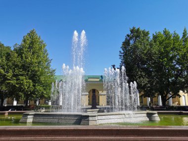 Gosin Avlusu yakınlarında bir çeşme, granit kâsesi Kronshlot şehrindeki Kronshlot kalesinin dış hatlarını andırıyor mavi bulutsuz gökyüzünün arka planına karşı..